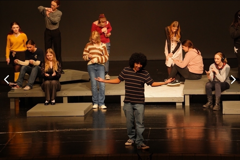 Students performing on stage. Focus is on one student in the center.