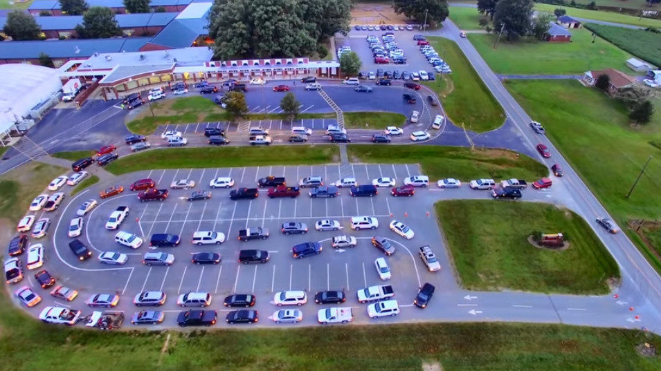 A busy school drop-off lane full of cars looping around a parking lot.