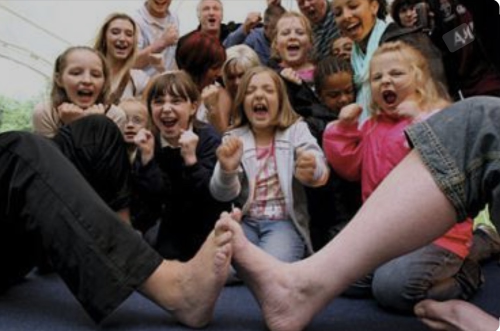 Children cheering while watching two feet with interlocked toes.