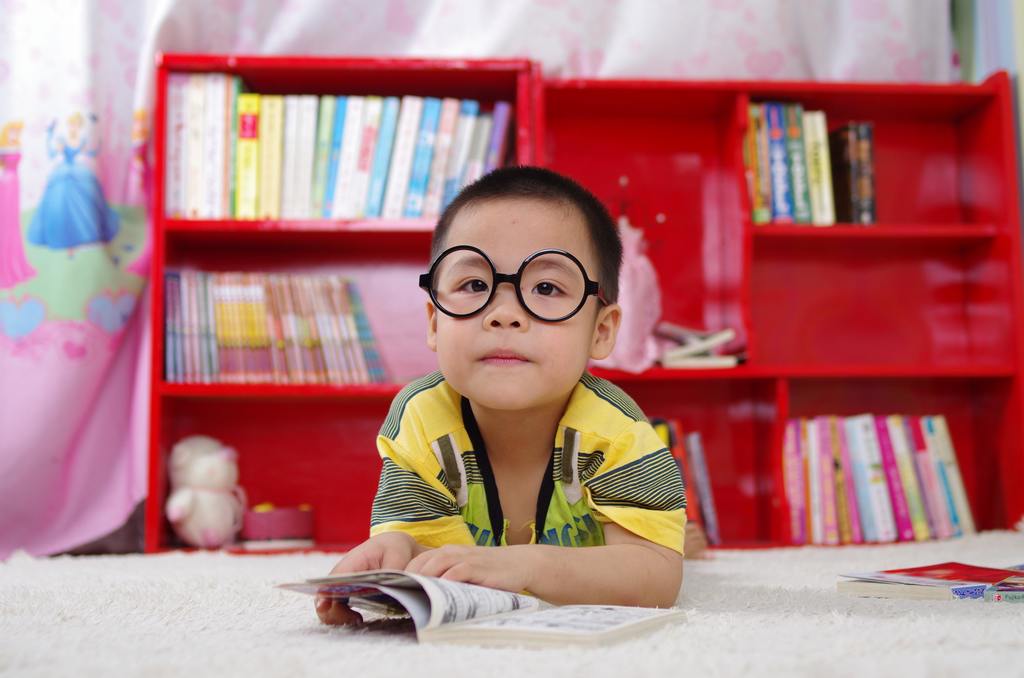 student kneeling in front of red bookcase reading a book