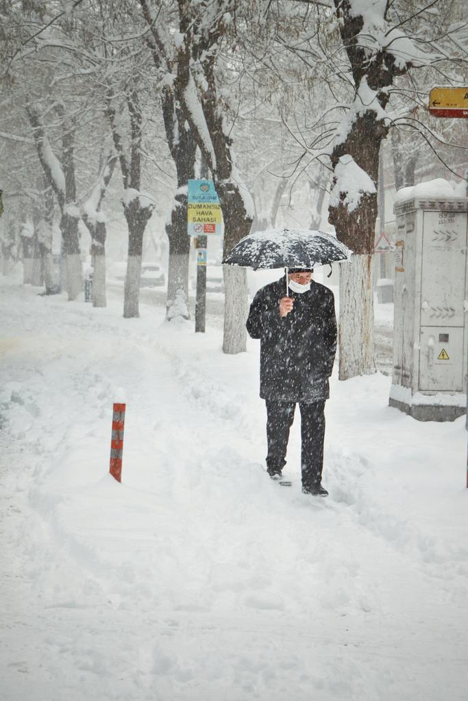 man walking in snow with umbrella