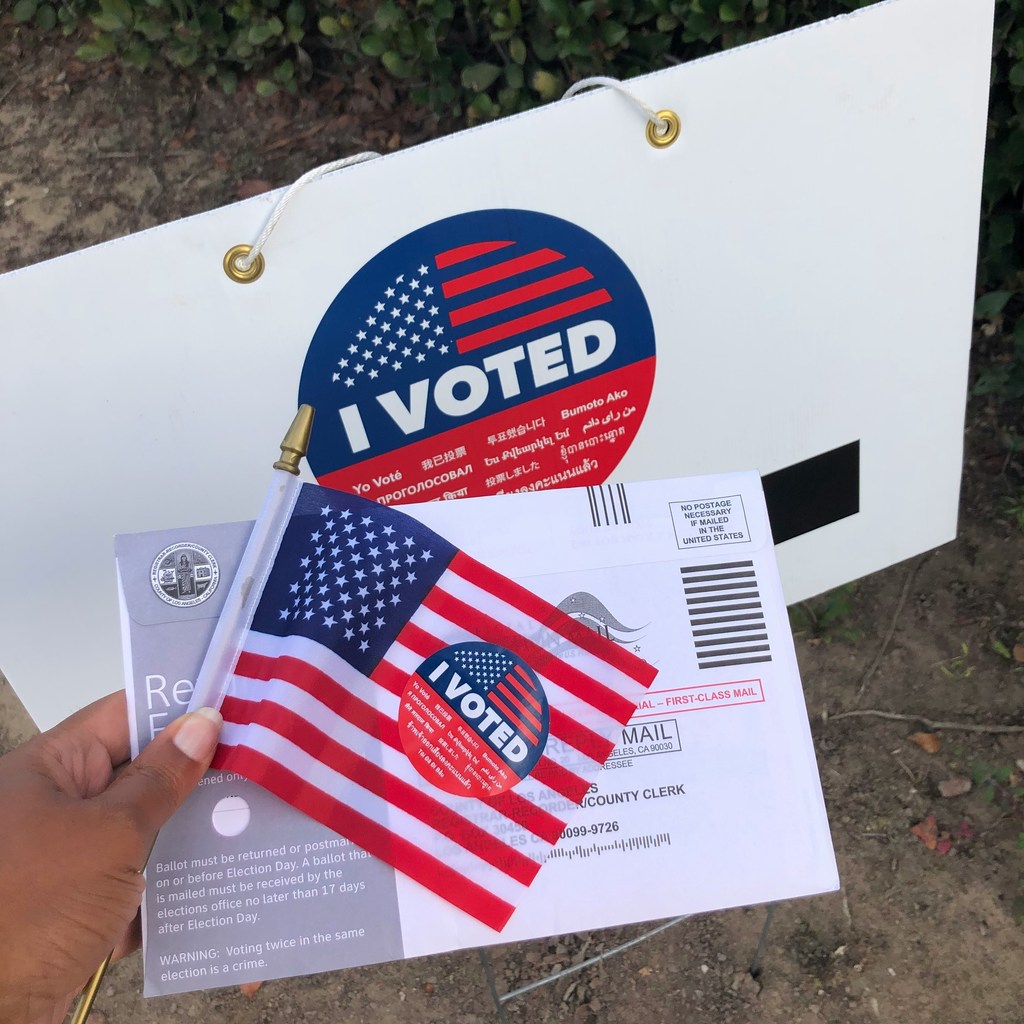 person holding american flag and voter card with i voted stickers.