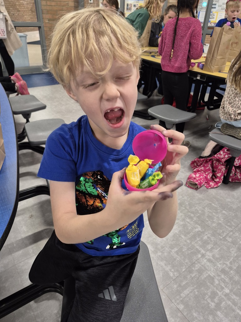 Blonde child in blue shirt and black pants holds candy in pink container. He looks up with mouth open.