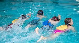 Four students swimming away from the camera with floatation devices