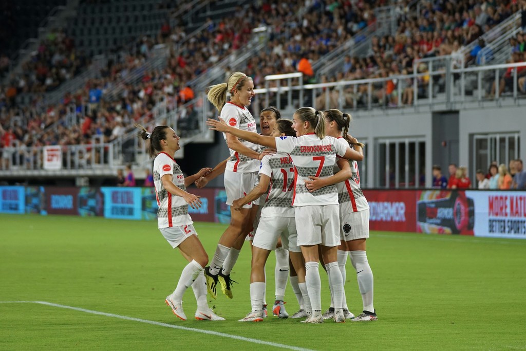 Soccer players celebrate on a field, surrounded by a cheering crowd in the background.