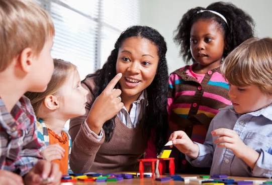A teacher sits with a group of elementary age students in the middle of a lesson. 