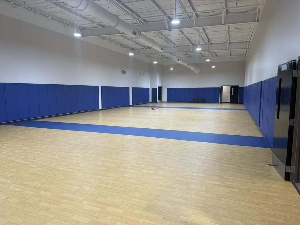 An empty gymnasium with a wooden floor and blue lines. The walls are white and blue.