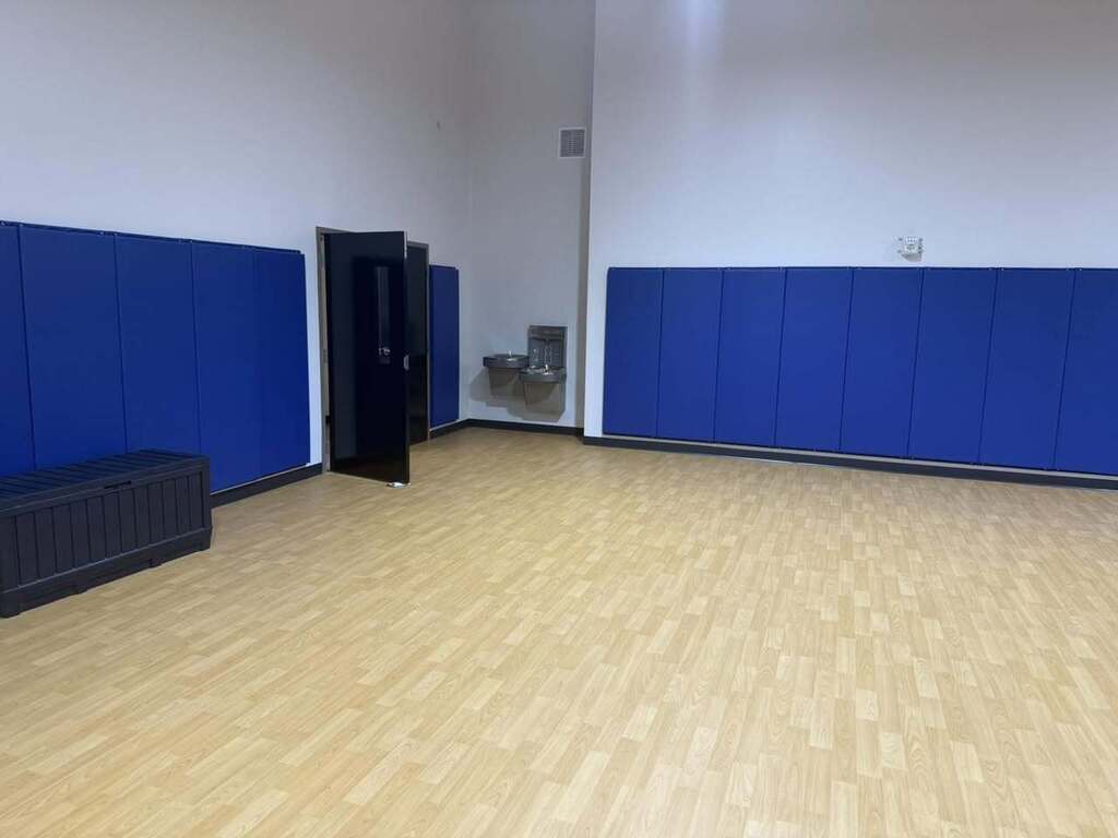 An empty room with blue partitions, a black door, a bench, and a sink. White walls and wooden floor.