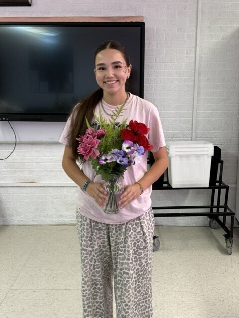 Person in pink t-shirt and leopard print pants holds a vase of flowers in a room.
