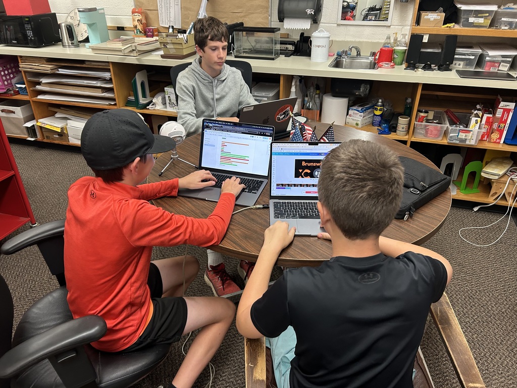 Three students working on a podcast around a table with computer.
