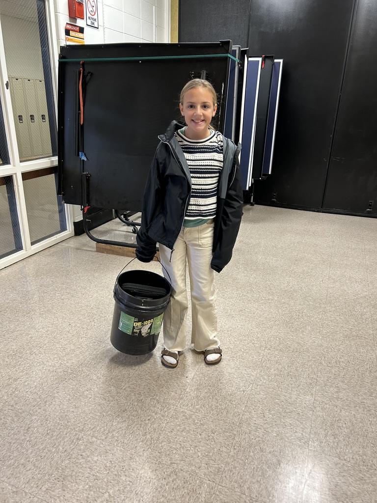 Student posing in a school hallway with unique bags as backpacks.