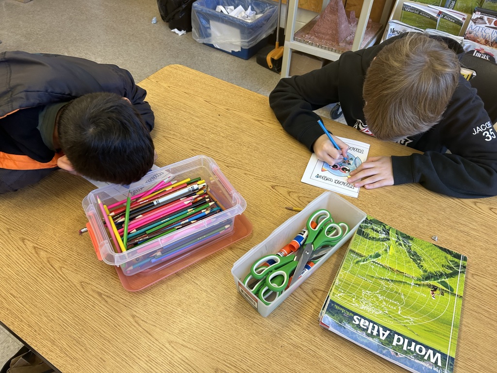 Two students working at a table on coloring thank you notes.