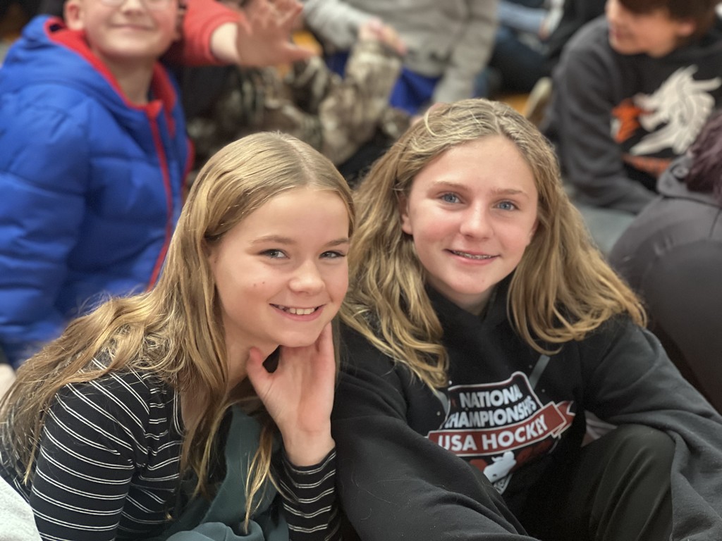 Two students sitting on gym floor at assembly.