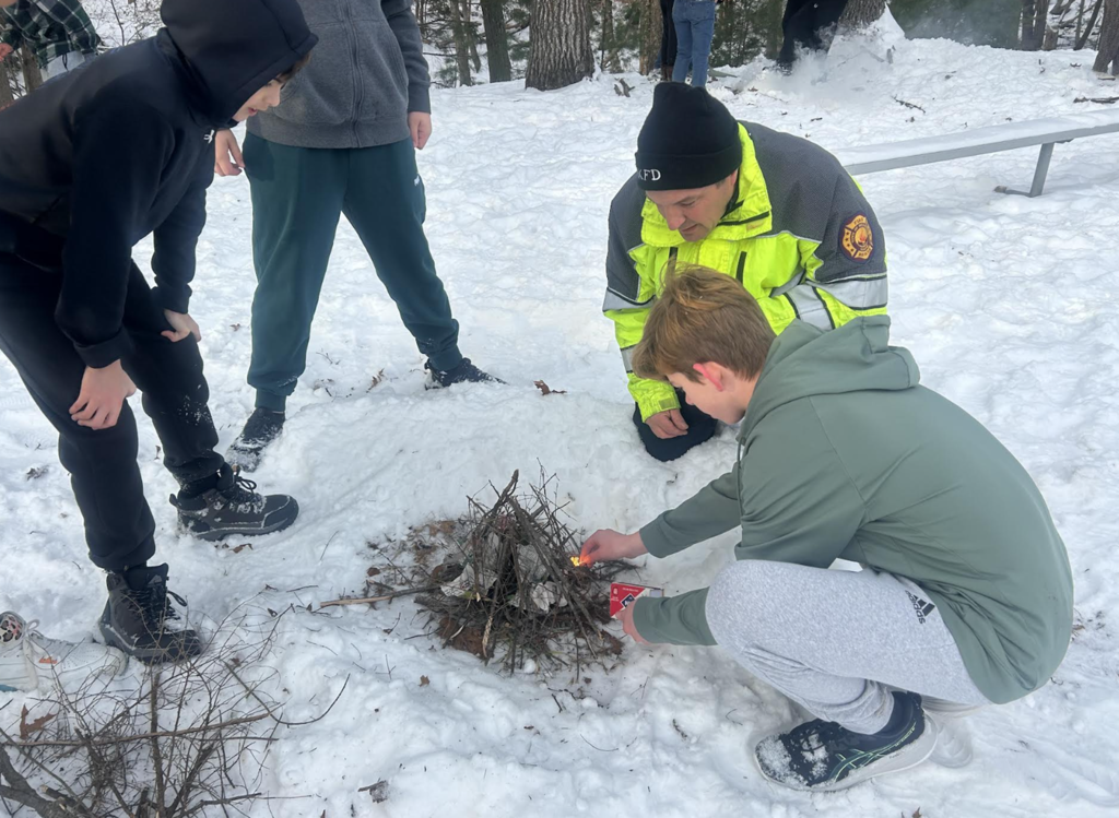 Three students and a Brunswick Fireman building a fire outside.