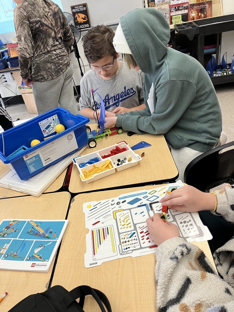 Two student sitting at a table building a LEGO sailboat.