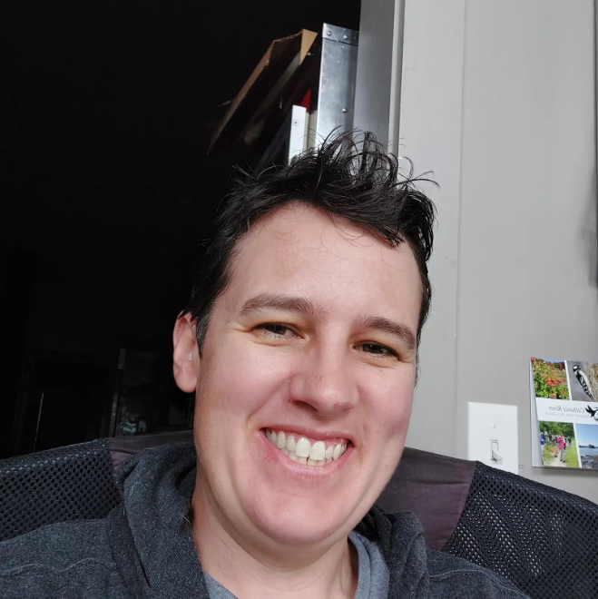 Woman with short hair and a big bright smile sitting in a chair.