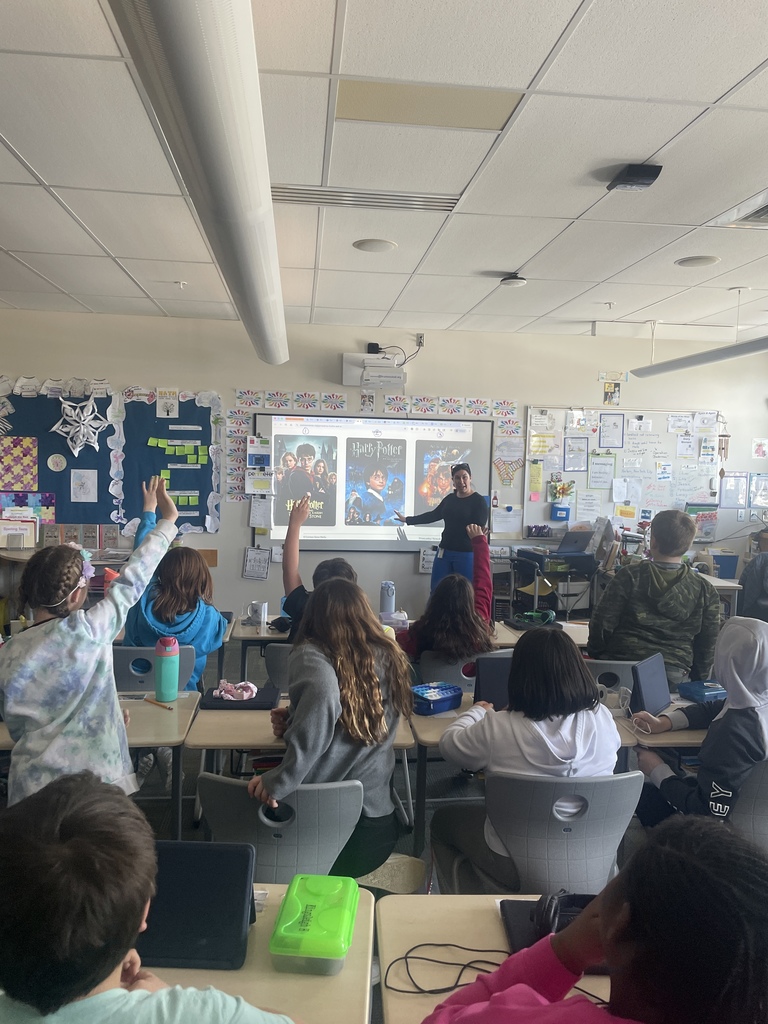 teacher at board and students raising their hands at their seats