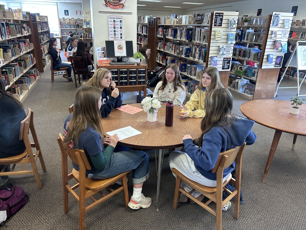 Group of BJH students sitting around a table with a BHS student having a discussion.