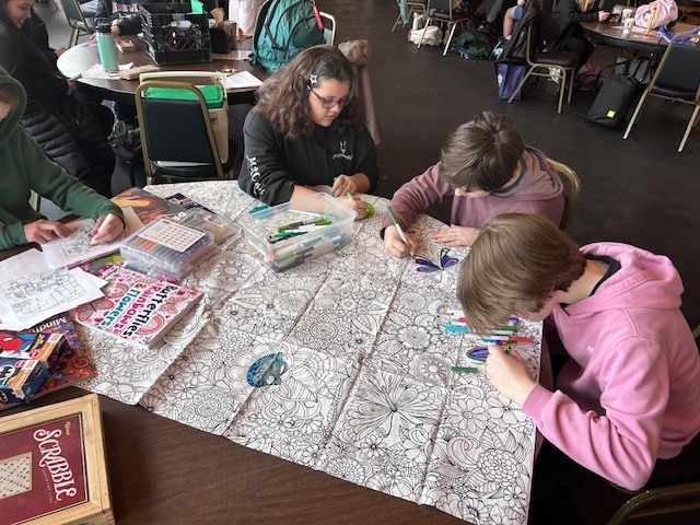 Three students sitting at a table color a large mural.