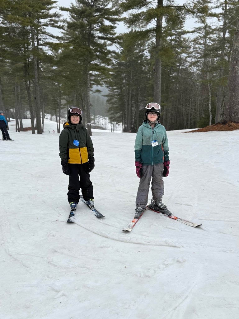 Two students on wearing skis on top of a ski mountain. 
