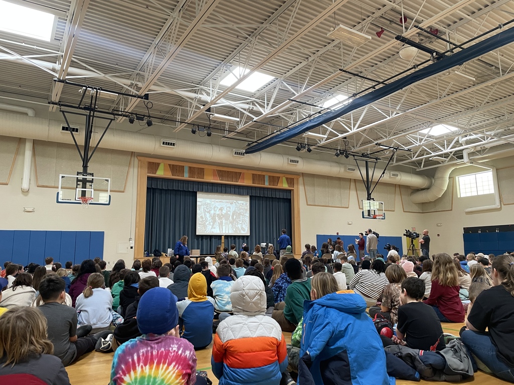 school gym full of students watching astronauts in space