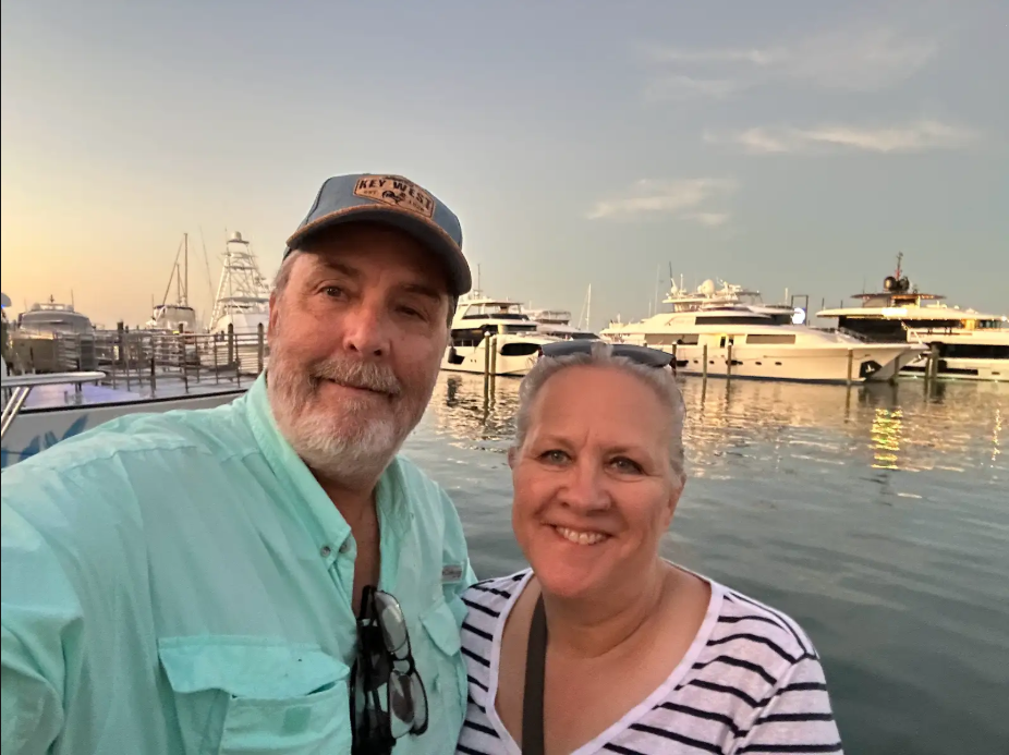Man and woman standing in front of waterfront with yachts.