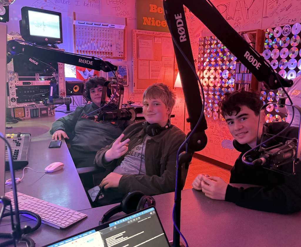 Three students recording a radio broadcast in a recording booth.