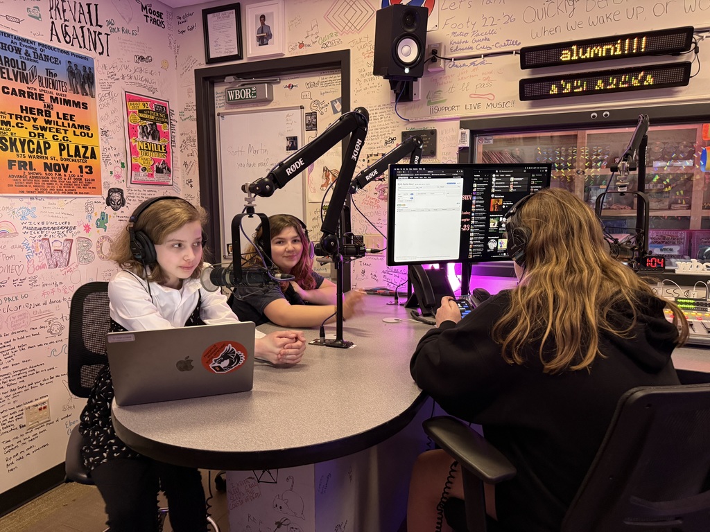 Three students sitting in a radio booth hosting a radio show.