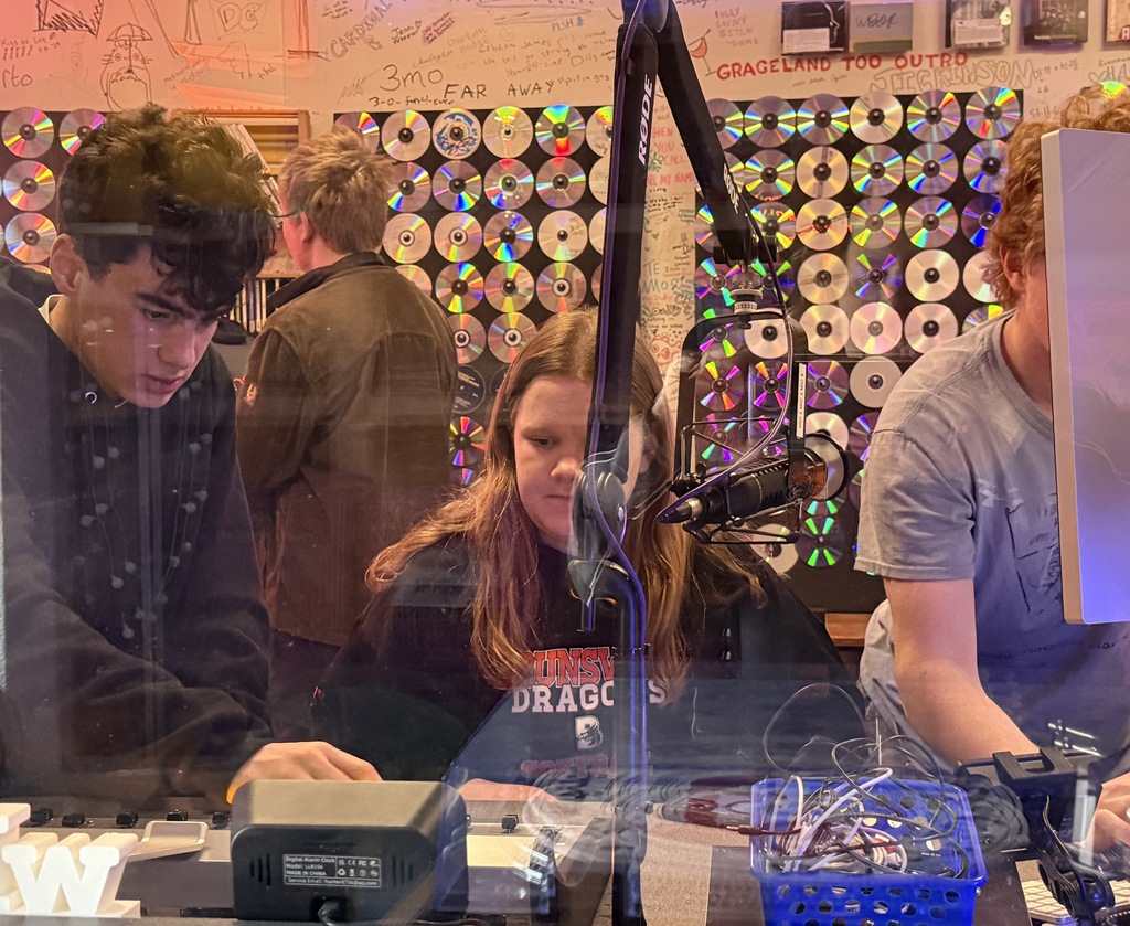 Two students learning how to do a radio broadcast in a recording booth.