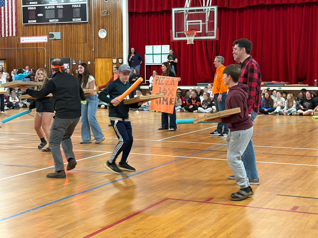 Students and teachers holding pizza boxes and pool noodles trying to knock thepizza box out of their hand.