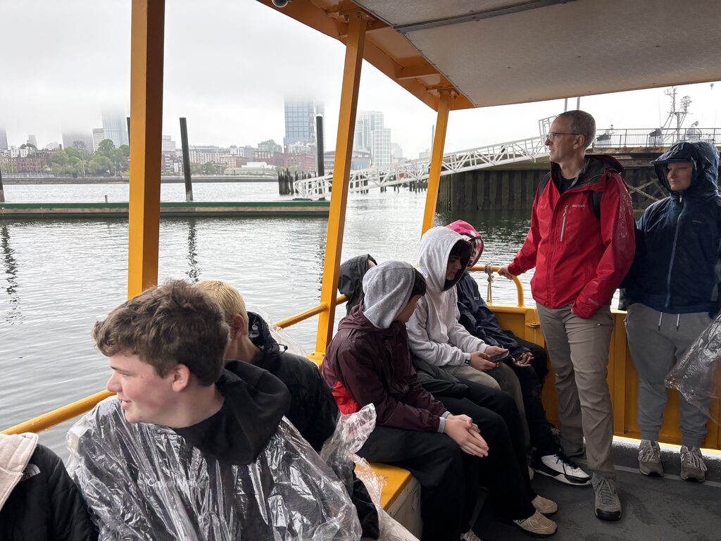 Six students and a teacher on a ferry looking out at the water.