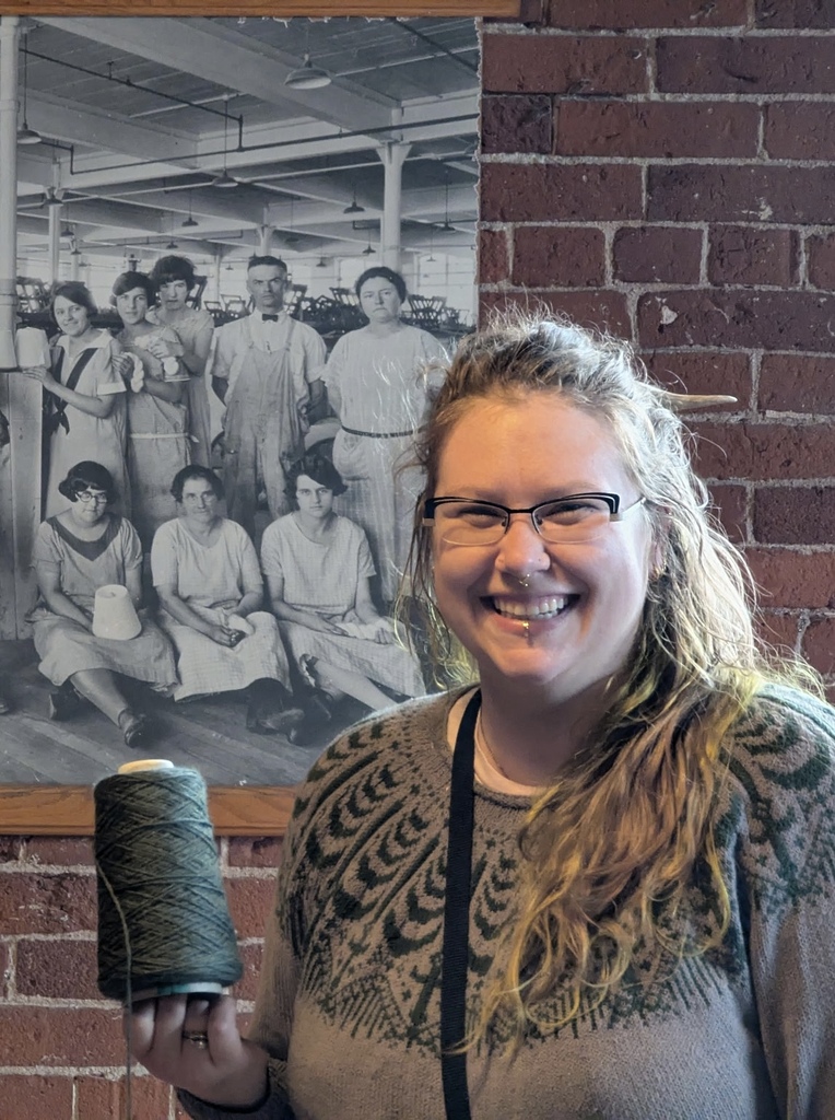 Smiling woman holding yarn in front of historical picture