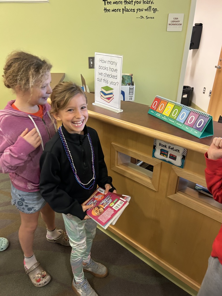 student holding book with big smile in front of the book check out