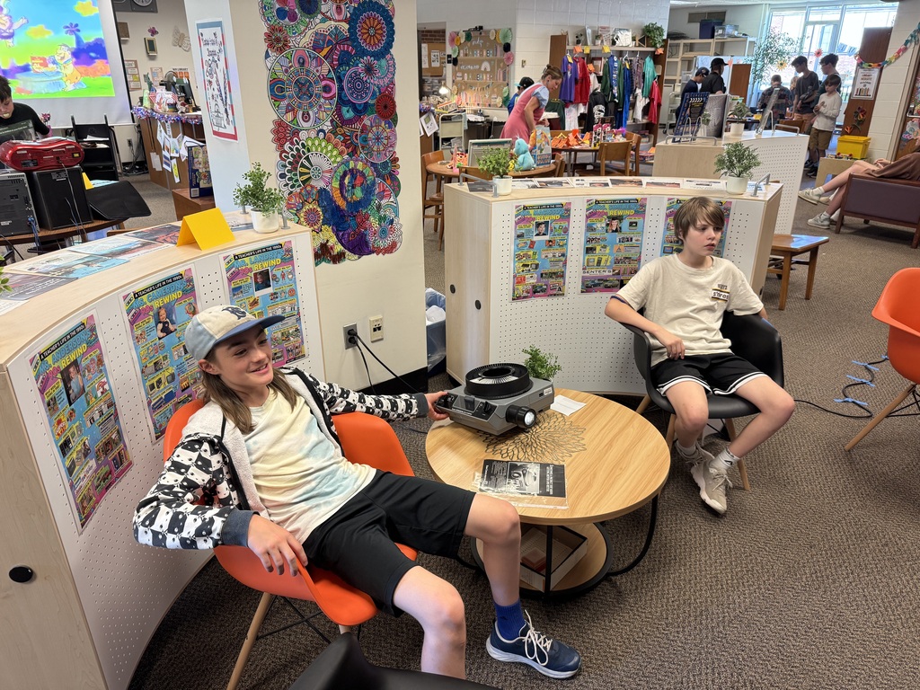Two students seated in the Library using an old fashion slide projector.
