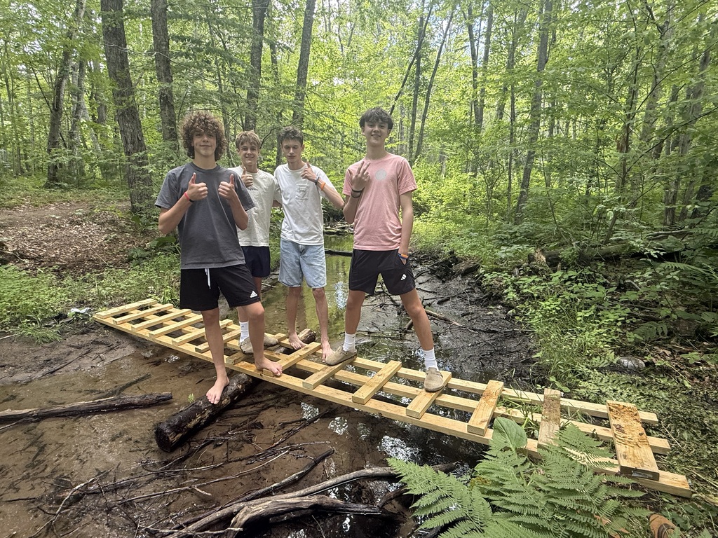 Four students standing in the woods on a ladder bridge they construction to cross a wet area.
