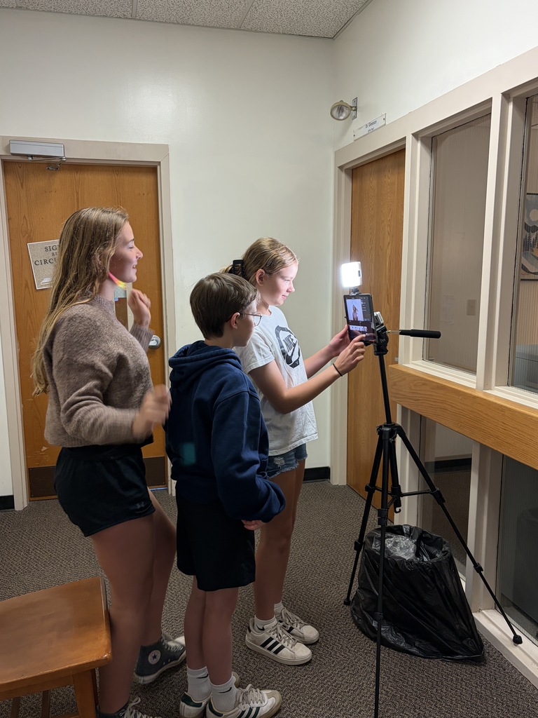 Three students standing infront of a camera reviewing theri recording. 