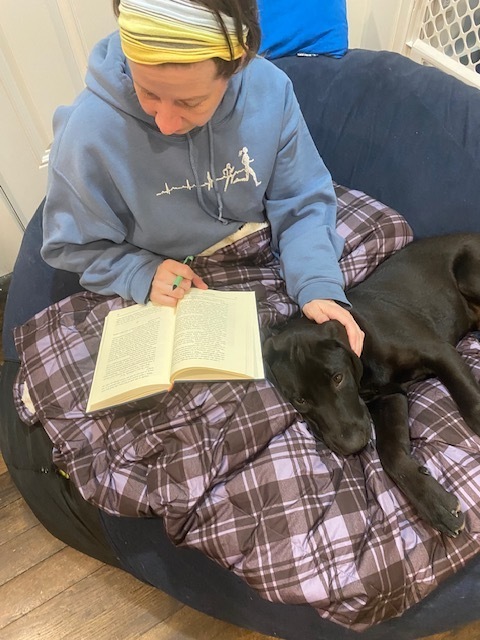 Woman sitting with a book and a dog on a beanbag