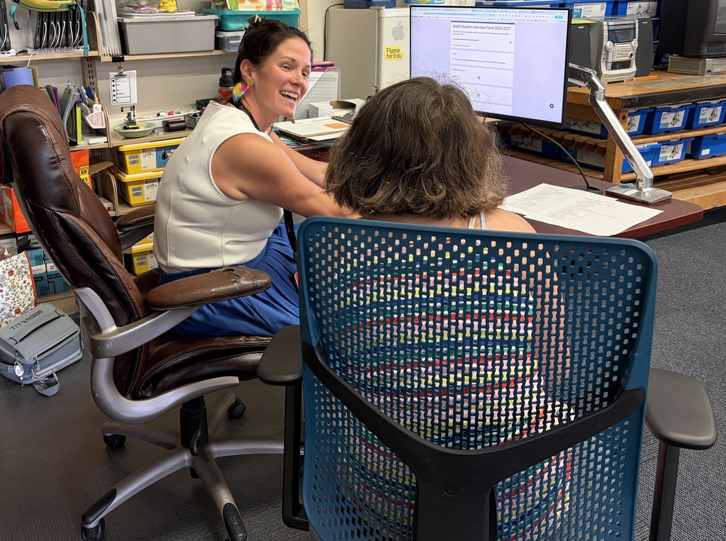Teacher and student sitting at a desk with a computer filling out a form.