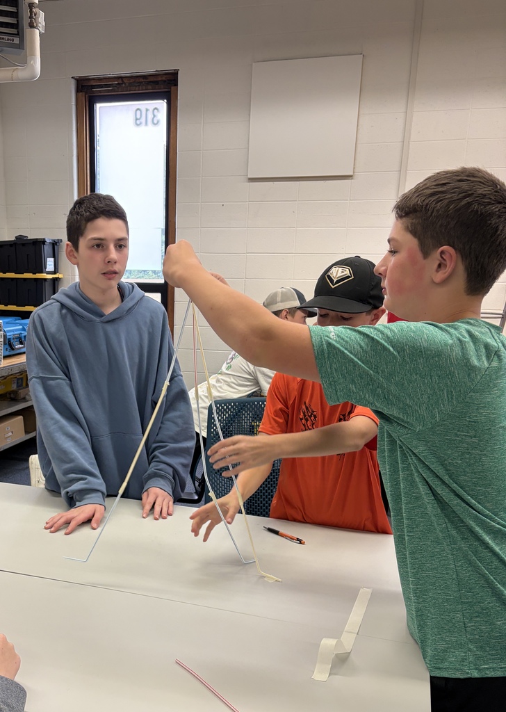 Three students standing around a table building a straw tower.