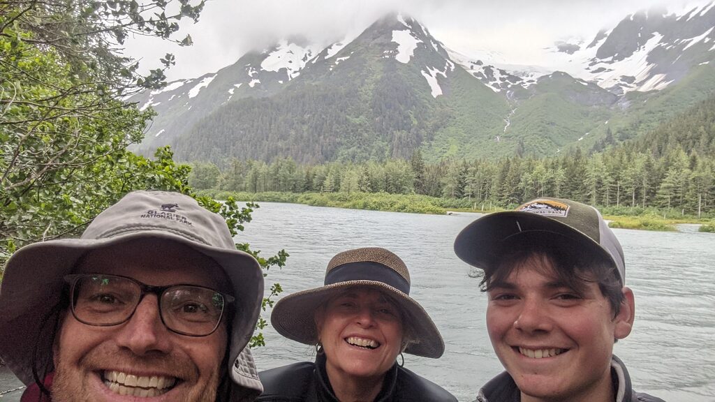 Family standing in front of waterway and mountains in the back in Alaska