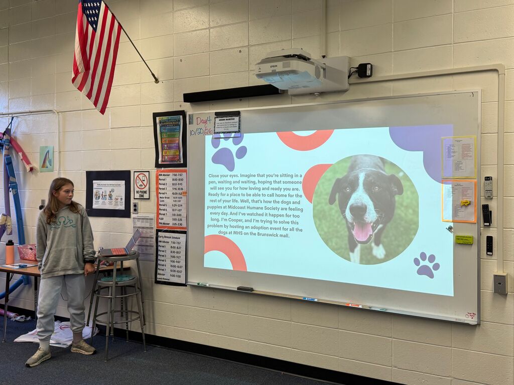 Female student stand infront of the class giving a presentation with a picture of a dog.