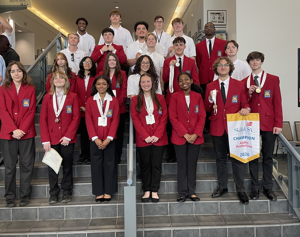 Students in red jackets and black pants, some holding medals and papers, stand on stairs.