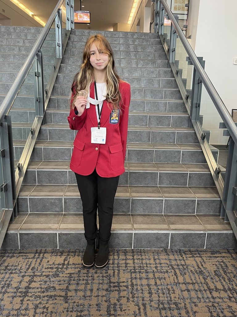 A student wearing a red blazer stands on a flight of stairs. They hold a white card.