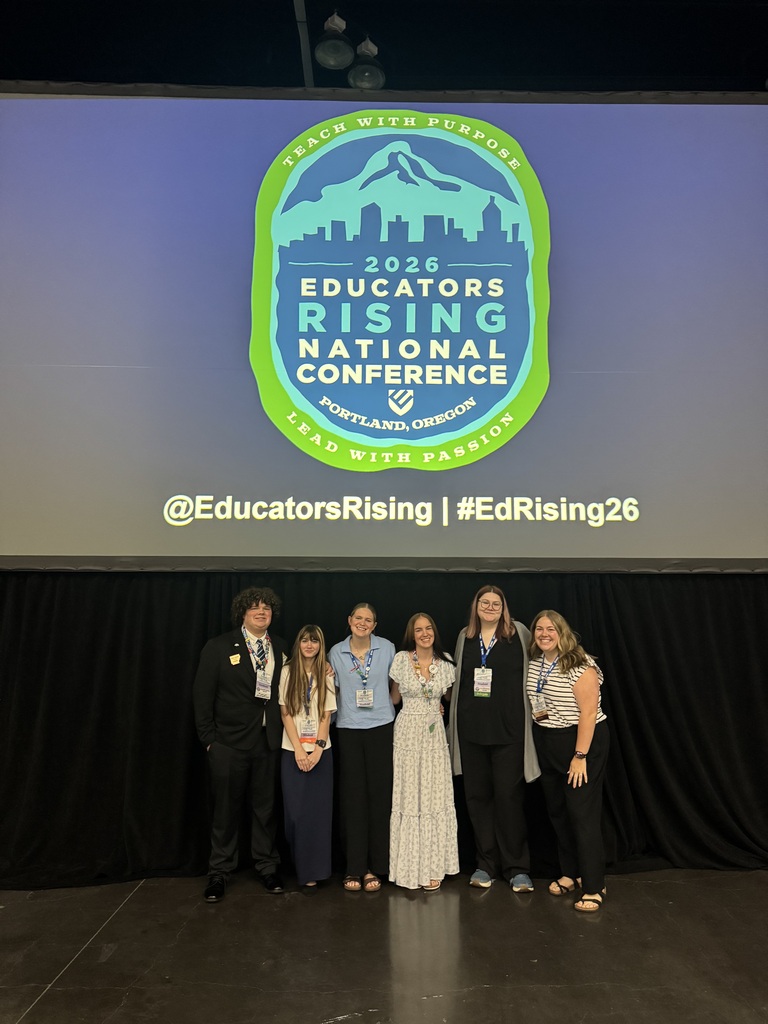 Five people stand on a stage, smiling, with a backdrop showing a logo for the Educators Rising National Conference.