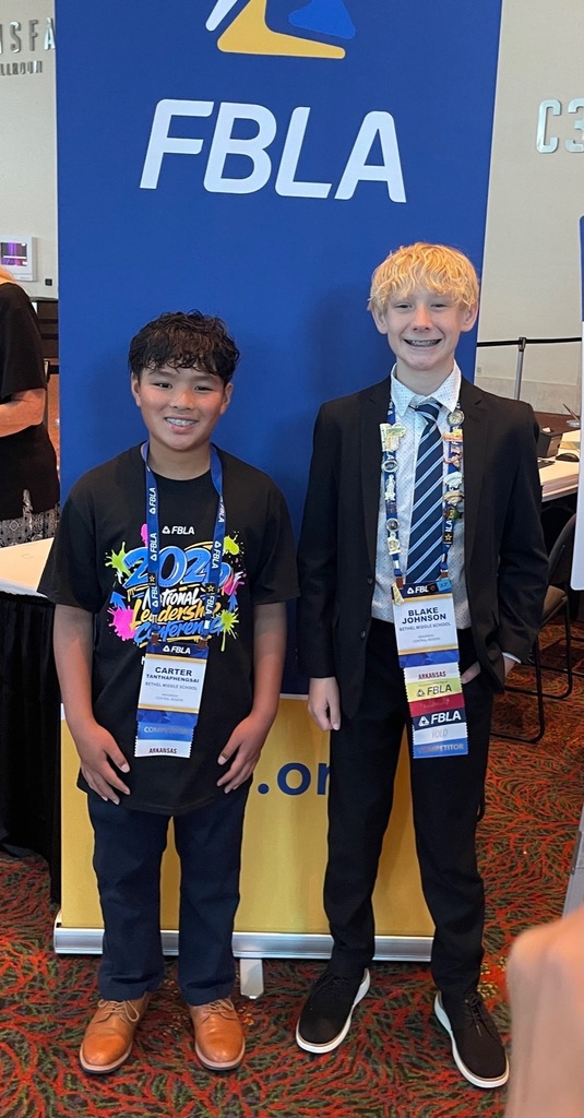 Two boys at a conference. One boy wears a dark blue shirt and brown shoes. The other wears a black suit and tie.