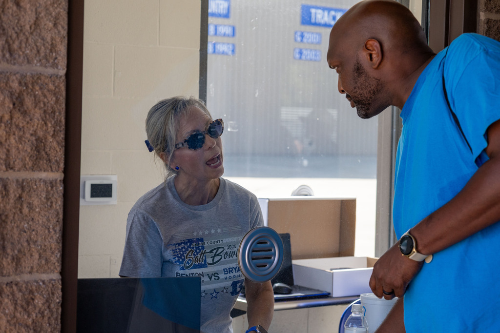 Man and woman standing outside a glass door; man in blue shirt, woman in gray shirt and sunglasses.