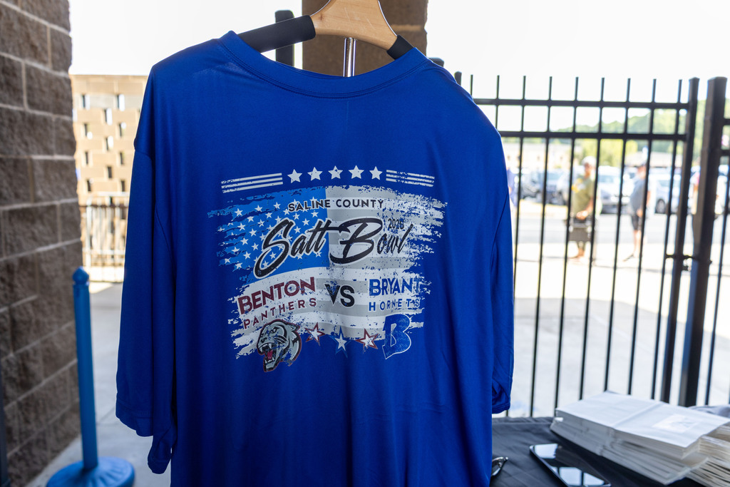 Blue Salt Bowl shirt with Benton vs. Branson design displayed near a brick wall and metal gate.