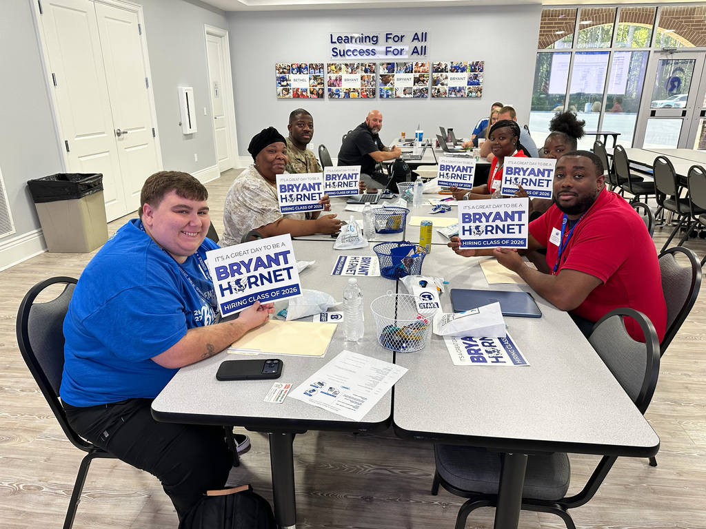 Group of people at a table with signs for Bryant Harnett. A banner on the wall reads "Learning for All Success for All."