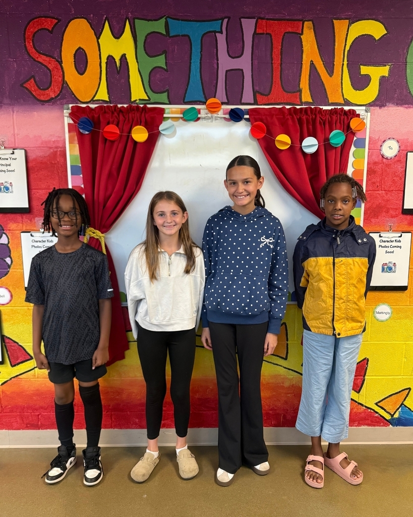 Four children standing in front of a classroom wall with a colorful backdrop and a sign that says "SOMETHING."