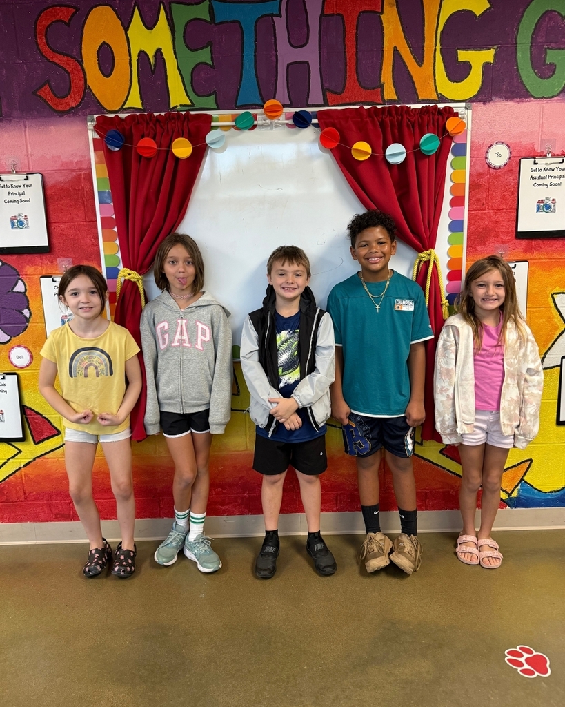 Five children in various tops and bottoms stand in front of a colorful wall with "SOMETHING" on it.